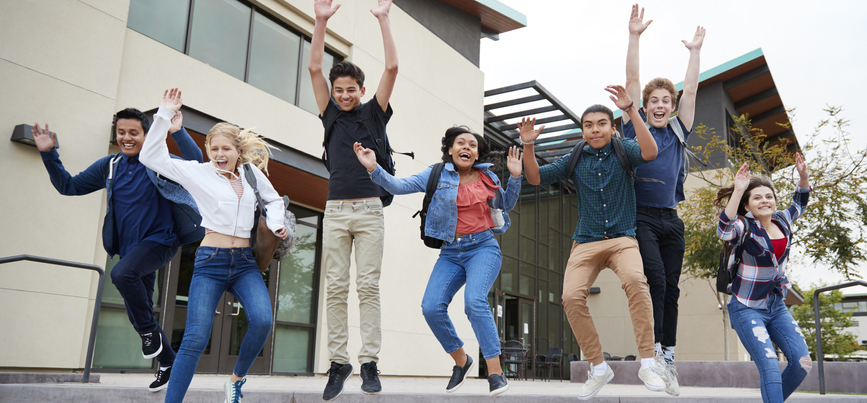 Group Of High School Students Jumping In Air Outside School Buildings